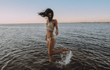 Woman stands in the ocean and raises one of her legs.